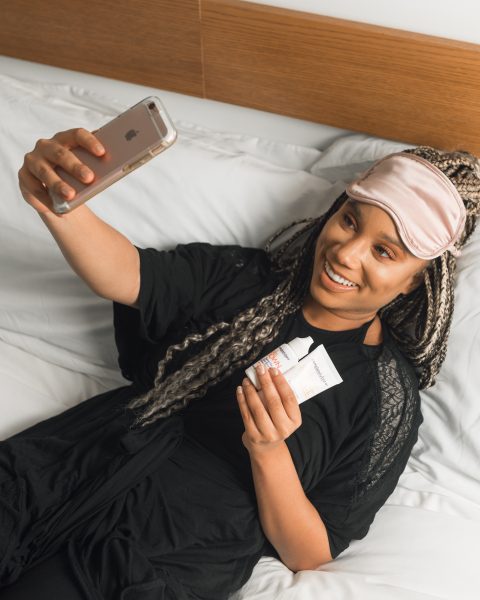Woman taking selfie wearing eye mask and holding products