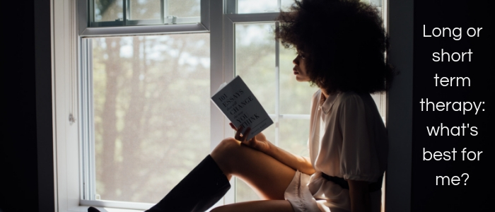 A woman sits on the window ledge, reading a book and looking outside