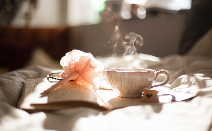 Cup of peppermint tea on bed with book