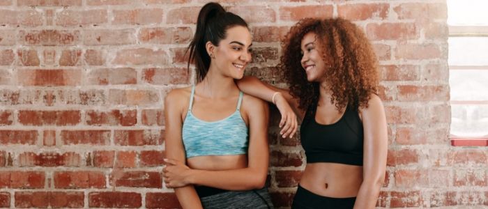 Two women smile together as they prepare to start in the gym