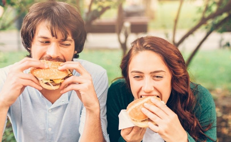 Couple eating burgers in park