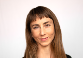 Image of a woman with brown hair and a black tshirt standing in front of a white background