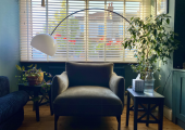 This is an image of an armchair in front of a lamp and window, with plants and a small table.
