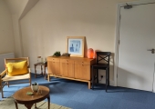 This is an office space with a beige couch, coffee table and chair as well as nice lighting.