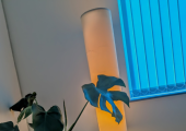Monstera plant sat on a white table in front of a tall warm glowing lamp in the corner of the room