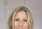 A psychotherapist wearing a while shirt and looking at the camera and smiling warmly