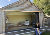 Emma, Positive Therapy Clinic, sits outside her counselling cabin, with the doors open in the sun