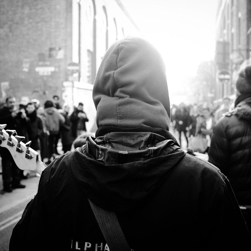 A young man walks alone in a crowd, standing apart from everyone else