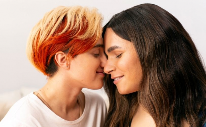 A transmasculine gender-nonconforming person and transfeminine non-binary person nuzzling