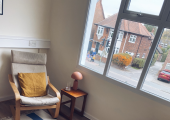 Two chairs sit opposite a single chair next to a wide window with a rug.