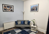 Image of a room with grey sofa, blue and grey rug, white coffee table with flowers on it