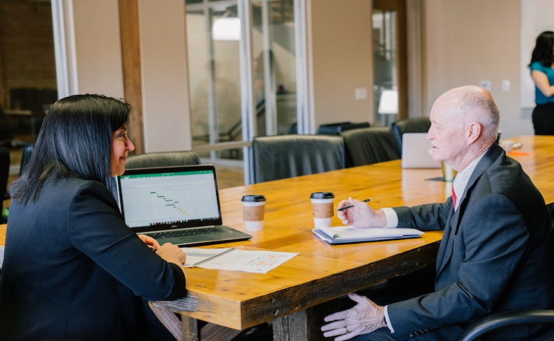 Male and female colleague sitting at laptop in boardroom