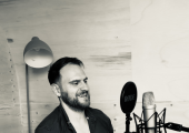 Adam Print laughing into microphone while recording The Coaching Snug podcast.