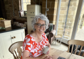 Nutritionist Lisa Picken sitting at the kitchen table working on laptop, holding cup of herbal tea