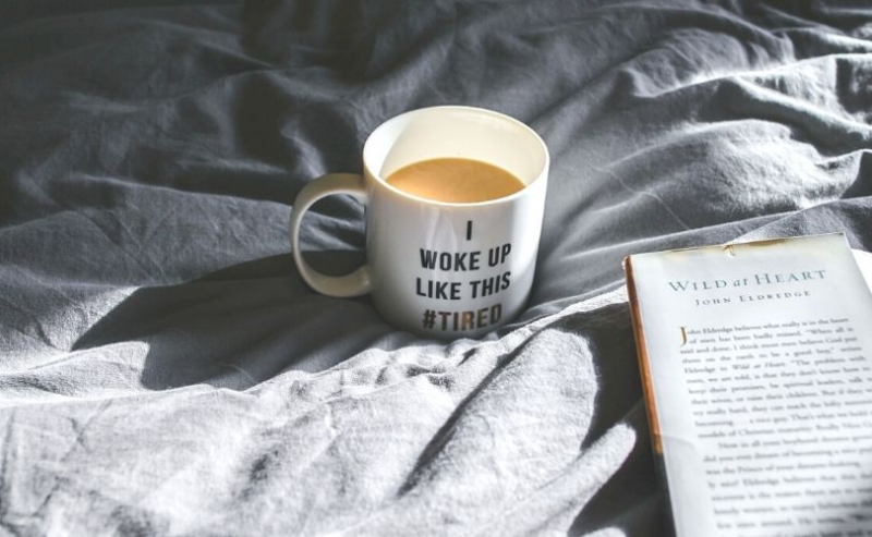 Cup of coffee and open book on bed